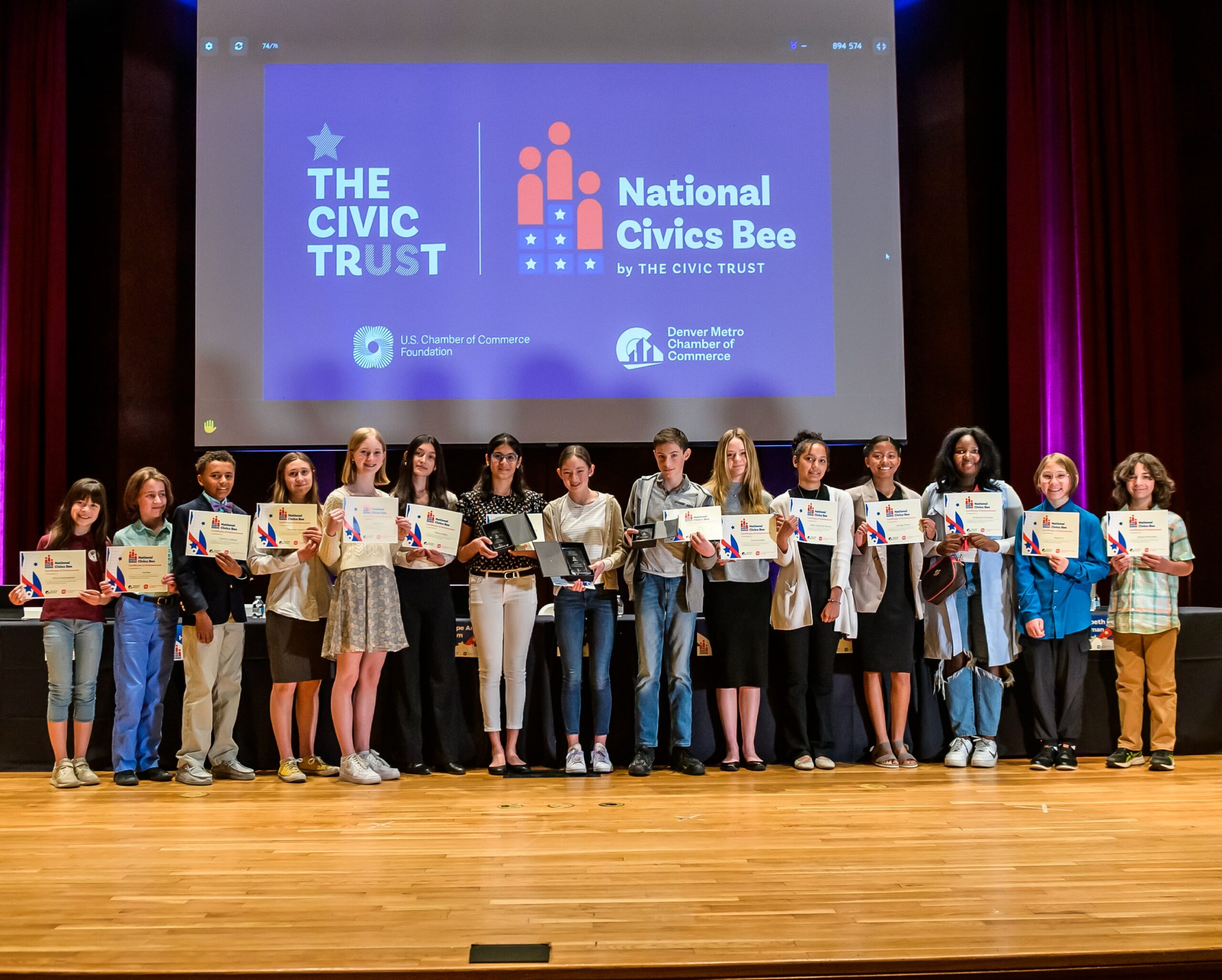 The 17 students from the Denver Metro Chamber's 2023 Civics Bee competition stand on stage with their certificates and awards.