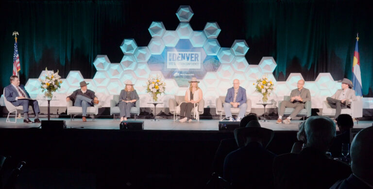 A stage is set with six panelists and one moderator looking over the crowd