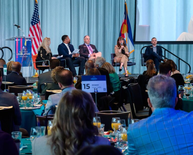 Colorado legislative leaders sit on stage for a panel discussion while an audience watches